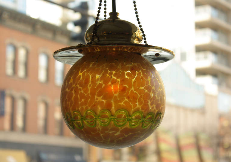 Klostermühle, Bohemia
This precious Vienna Secession hanging lamp, made by Loetz Witwe, has a glass globe created by a highly-skilled craftsman. The iridescent globe is of golden hued glass, with a layer of amber-shaded mottling, and banding in