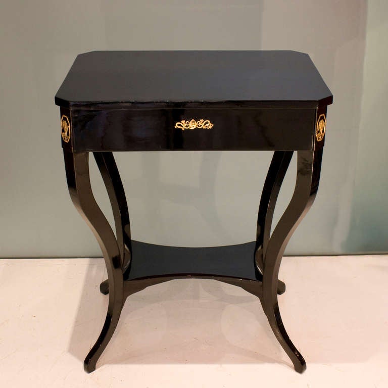 This Biedermeier side table in ebonized wood has four saber legs joined by a delicate shelf. Original brass mounts sit at each corner.

The full drawer in the apron has the original lock and key in perfect working condition.
