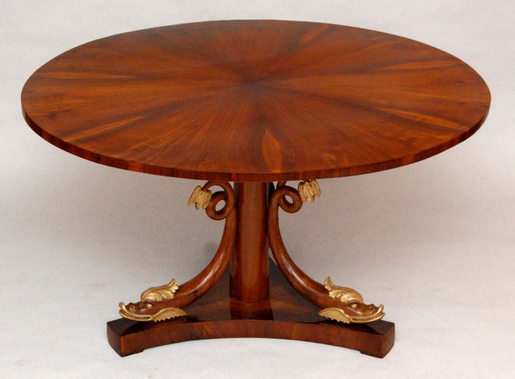 Neoclassical centertable with gilt dolphin scrolls and fine walnut star-veneered round top supported by an upward tapering column. Extending scroll-shaped dolphins with raised tails rest on the tripod base. A prime example of early