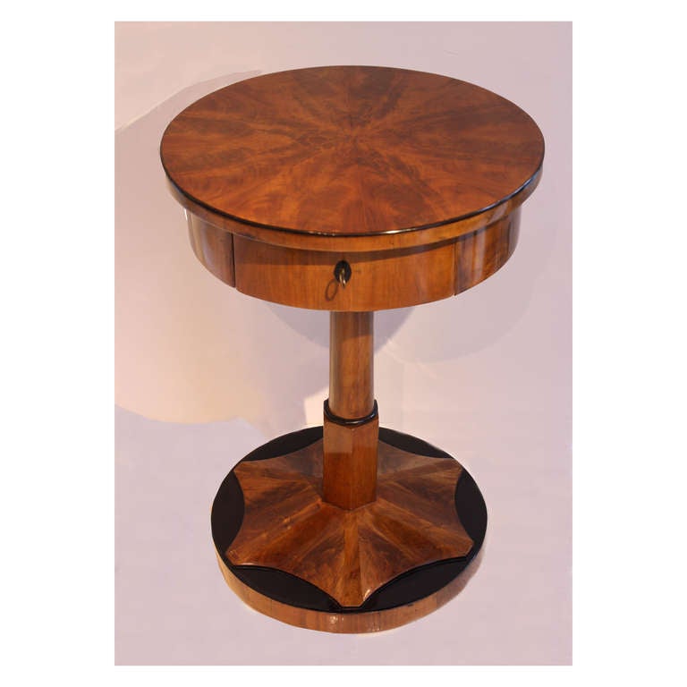 A delicate round side table skillfully crafted the the Josef Danhauser workshop. This table features a three-dimensional starburst sitting on a round, ebonized base. The circular, burled walnut veneer is outlined by ebonized edges. A full drawer in
