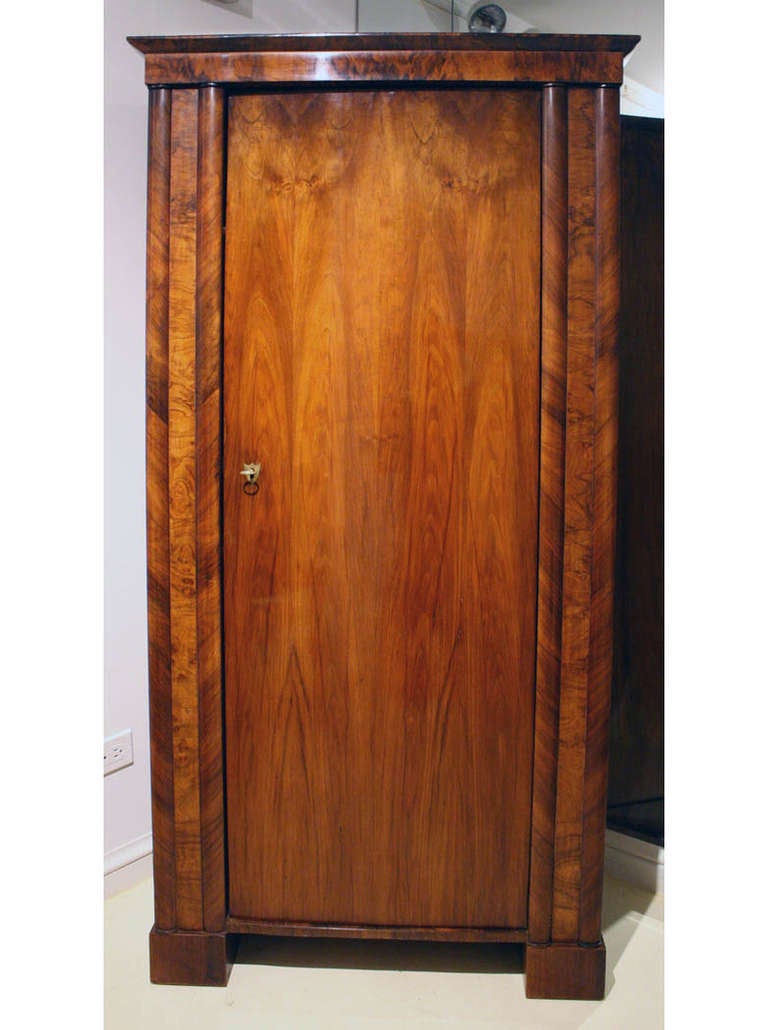 The elegant structure of this single-door Biedermeier armoire speaks for itself. The beautifully figured walnut-veneered door is flanked by double pillars, of which the veneer is applied in matching mirrored diagonals. The inside features 3