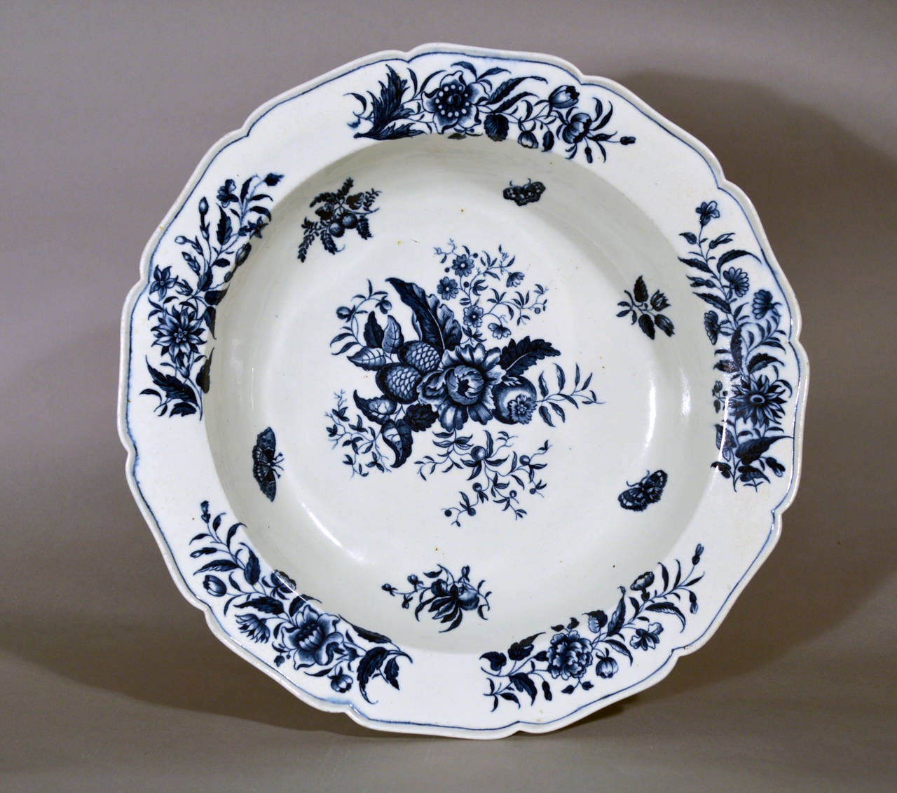 A massive first period Worcester underglaze blue porcelain pine cone pattern basin, with shaped everted rim, printed in blue with insects and various arrangements of fruit, flowers and leaves. Printed shaded crescent mark in underglaze blue on the