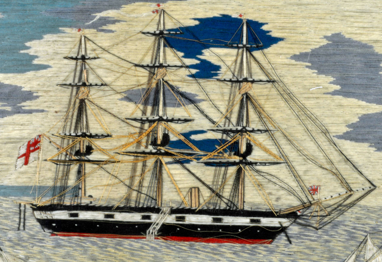 The sailor's woolwork known as a woolie has a wonderful serenity to it as it depicts a Royal Navy ship, probably a square-rigged sloop.  The ship is anchored close to shore, a jack flag on her bow, a ladder into the water can be seen on her port
