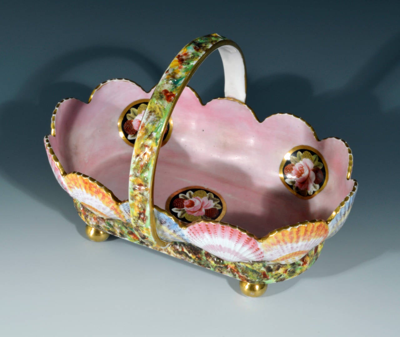 The interior of the footed oval basket is finely decorated with five circular panels with a gilt border containing a grouping of well painted flowerheads including roses all on a pink ground.

The exterior is formed by alternating moulded sea