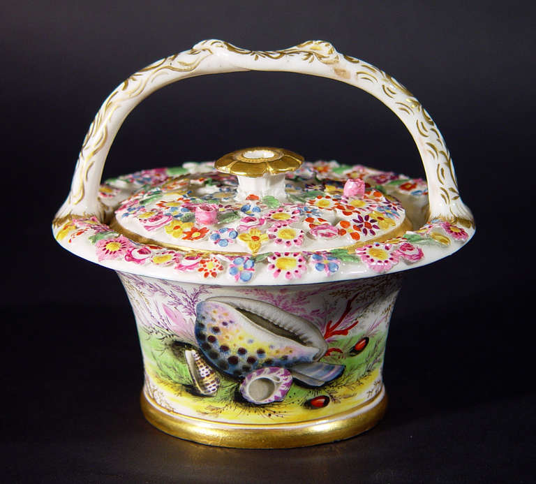 The circular basket is finely painted with two large panels of sea shells and sea weed between a painted gilt seaweed design.  The openwork cover and rim of the basket are moulded and brightly painted with flowers, topped by a gilt flowerhead