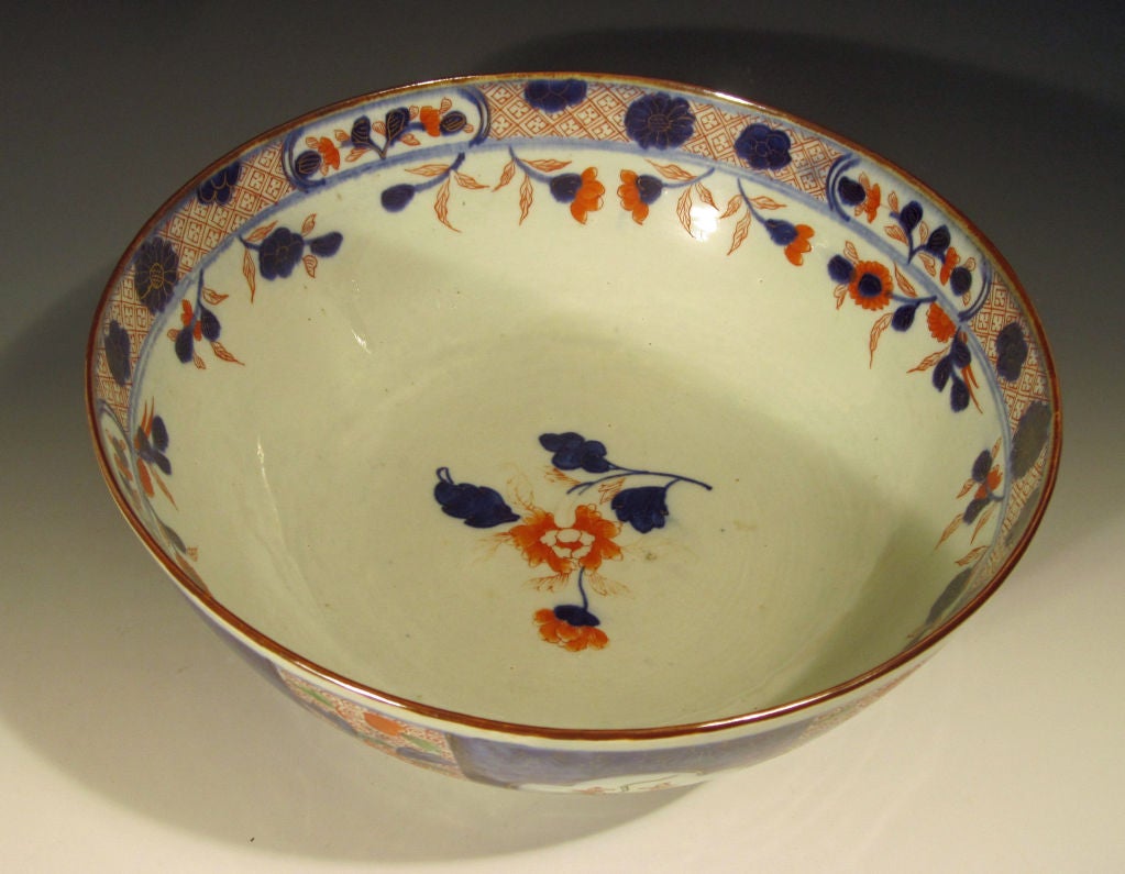 The punch bowl is decorated on the exterior with alternating panels of mirrow blue overlaid with gilt flowerheads and petal shaped panels of iron-red flowers and green stems and panels of iron-red scroll-work with large flowers in underglaze mirror