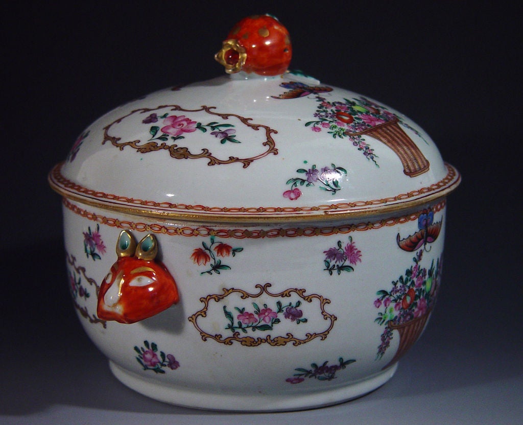 The tureen and cover are decorated in fine famille rose enamels in the Meissen-stypedepicting on each side a tall wicker basket filled with fruit and flowers with a large butterfly hovering above.  To each side of the baskets are large shaped panels