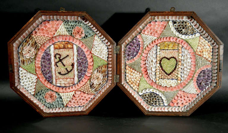 
The large double valentine is in an octagonal, glass fronted hinged wooden box. The left side depicts an anchor in red shells entwined with rope in small green shells.  The right centre depicts a heart, the outline also in red shells and the