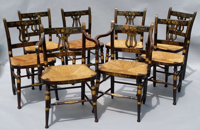 A Pair of Armchairs and Six Chairs, 

The chairs with lyle-shaped back and rush seats in black and red with stenciled design and gilt highlights with a flat crest rail at top and a thinner lower cross rail with a lyle design between. The turned