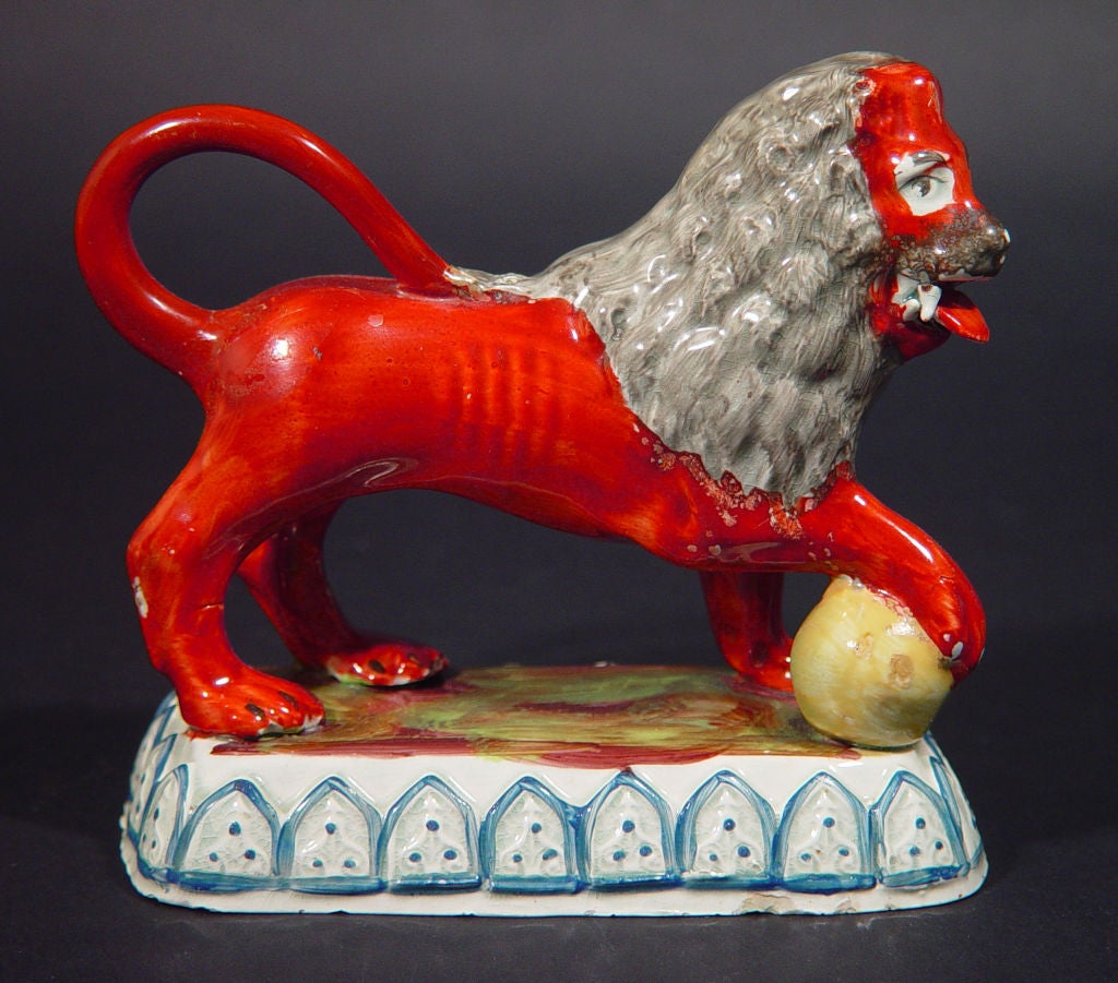 The charming lions are in a striking deep red with gray mains, each with a paw raised on a yellow globe- one with its right paw and one with its left..  The rectangular hollow bases have applied crenulated shields around the base edged in blue.  The