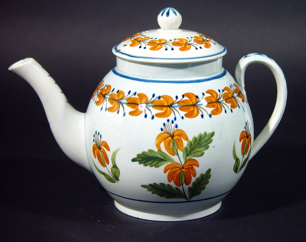 A charming folky fresh pottery teapot decorated with flowers in distinct orange and green.