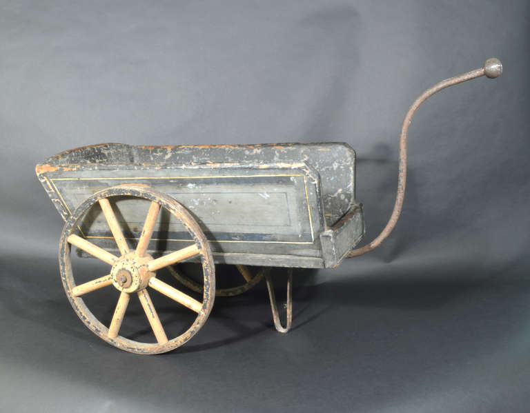 A charming flower barrow with an old blue paint finish, two small goat cart wheels and a shaped metal handle and a v-shaped metal support on the underside.  An antique metal  metal plate on base of the base to hold flower pots.