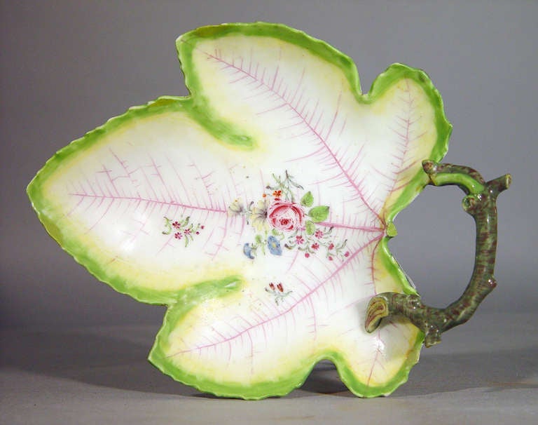 The dish in the form of a leaf painted in the centre with a floral bouquet superimposed on a network of veining, the rim is serrated.