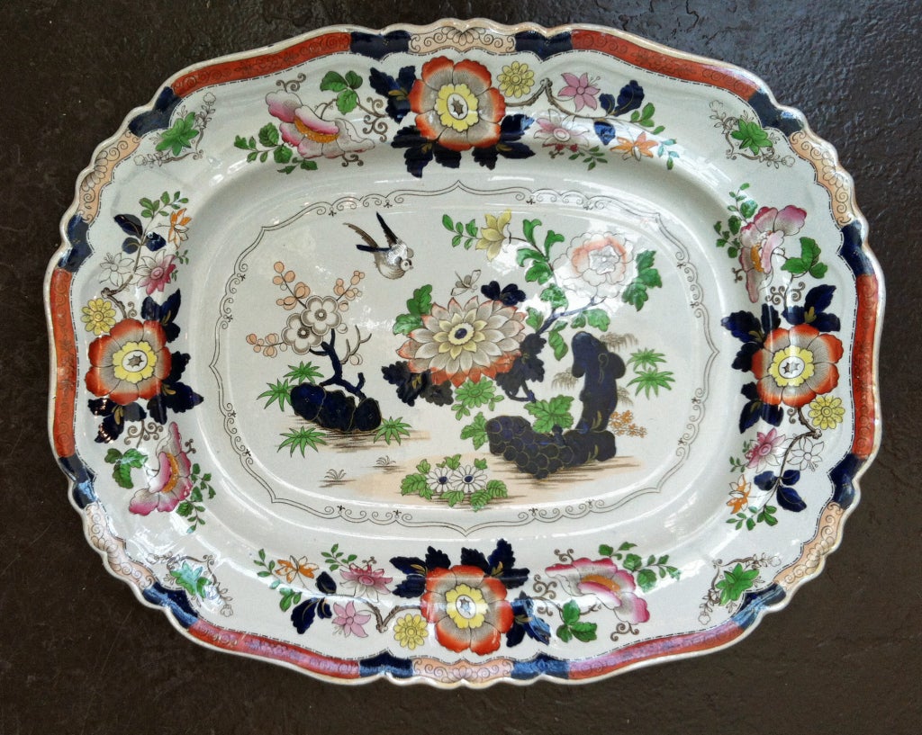 The large shaped dish with a slight recessed central well and an unusual recessed rim is decorated with a design in Imari colours of a bird hovering above a chrysanthemum flower issuing from blue rockwork in the Chinese style.

Mark:  New Stone