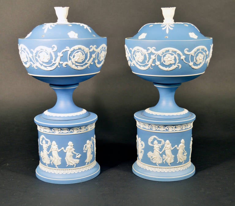 The urns, covers and stands are of white jasper with a blue dip ground and applied white decoration. Each decorated with dancing muses. 
Marks: One vase: ADAMS. EST..1657 & impressed letter M & J.C. & scratch 65
Second Vase: ADAMS/ Est. 1657;