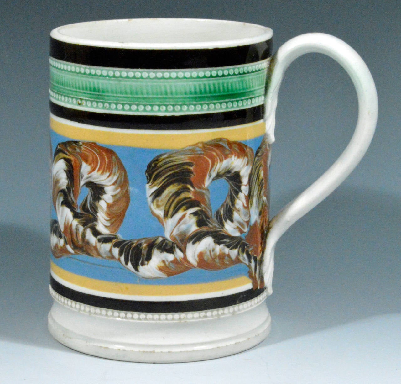 The tankard with a central band of earthworm design on a light blue slip ground framed between continuous bands of yellow, white and brown.  The rim has a wide band of brown above a green band with moulded pearls.