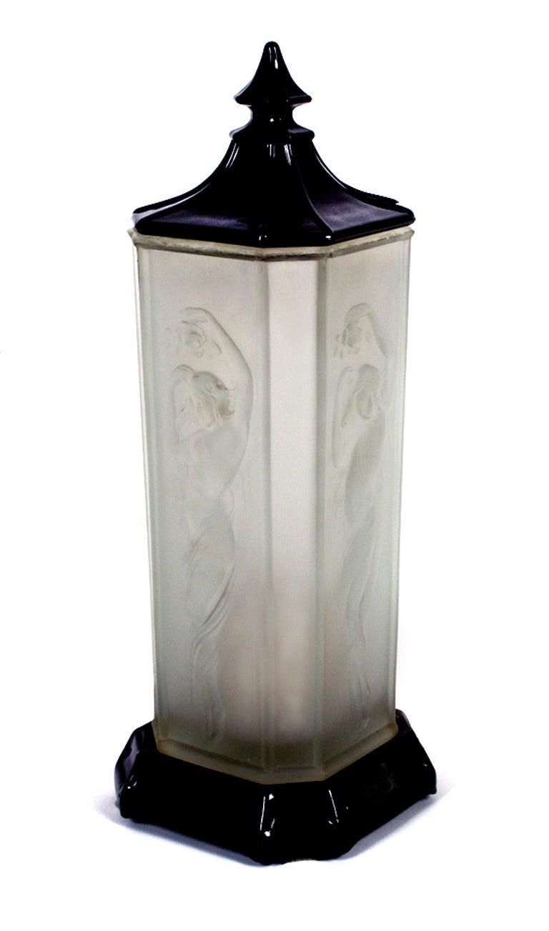 American Art Deco period lidded accent lamp by Tiffin Glass Company, circa 1920s. Base and top are black glass, body is satin finish with nude female dancer in relief on all four sides; mitered corners. 

Tiffin Glass Company of Tiffin, Ohio began