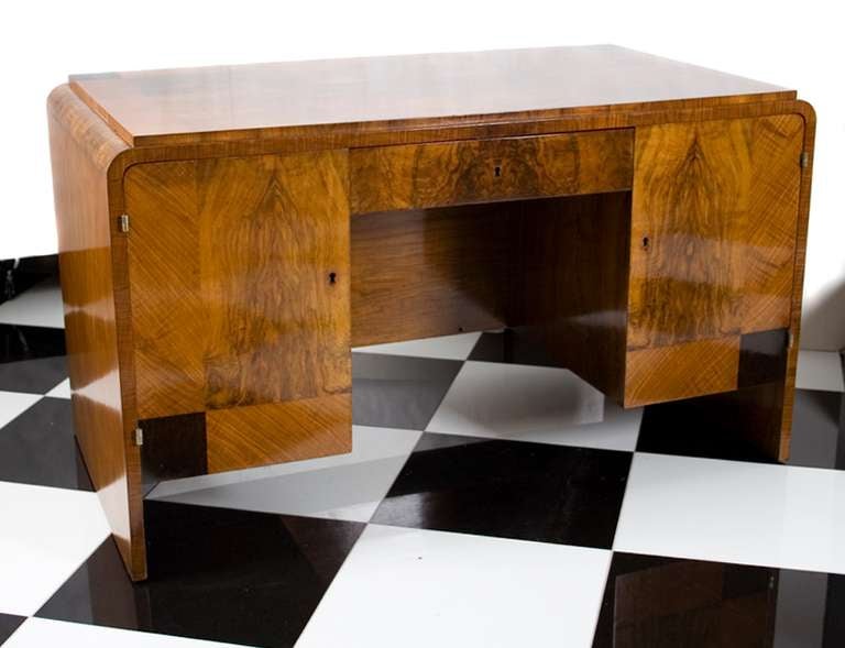 French Art Deco period walnut "waterfall" style desk with ebonized inlay. Center front drawer; two side doors with sliding drawers. Back of desk two shelves. Ebonized detail on bottom front corners and top. This piece is en suite with