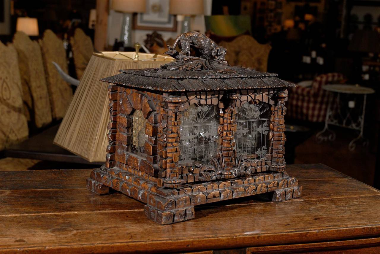 A Tantalus is small wooden cabinet fitted with decanters and cordial glasses.
It locks to secure the contents from servants and children. This Tantalus is expertly carved to appear to be a lovely stone cottage with a retriever on top, protecting