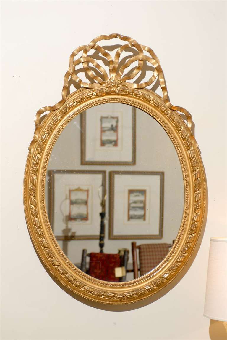 This fabulous Louis XVI style mirror has a Flying Bowknot Crest.  It also has rolled ribbon and a floral motif around the frame. It has beaded molding.