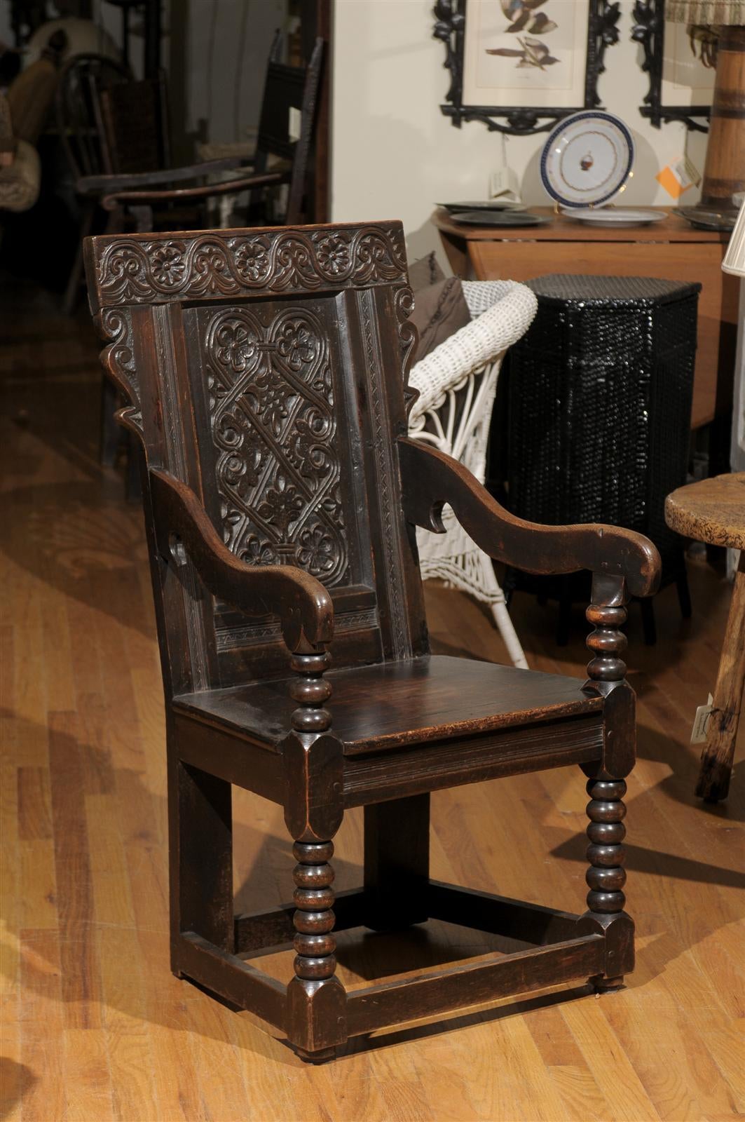 This English chair carved in low relief. This solid wood chair is reminiscent of Elizabethan period. The chair has a back panel detailed with cross hatch design separating stylized rose and forms of nature. This detail is repeated in the tool back