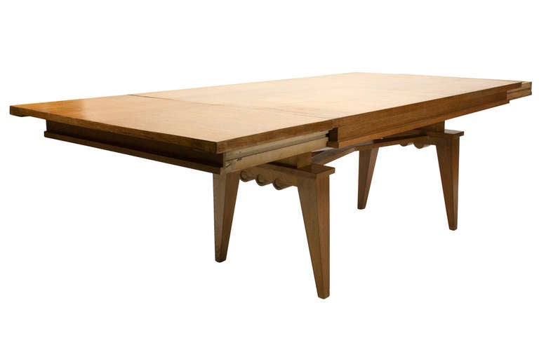 A midcentury oak extending dining table with X-form medial stretcher extending to a scalloped apron and finished with tapered legs.

Measurement includes two leaves, each 19.5'' W x 39.5'' D.