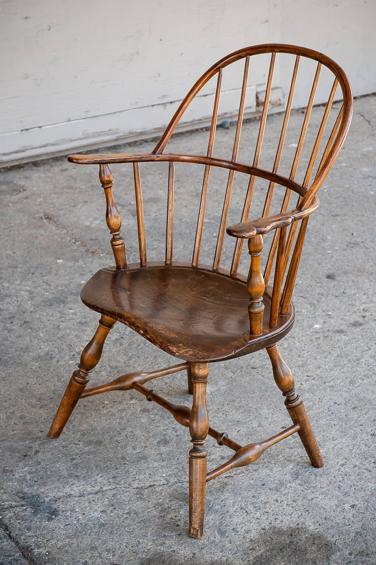 Early American sack-back windsor armchair.
Possibly Philadelphia, likely dating to 1770-1790.
Knuckle form arm-rests. 
Rising on boldly turned legs conjoined with likewise pronounced joinery. 
Exceptionally sculptural seat with rich surface