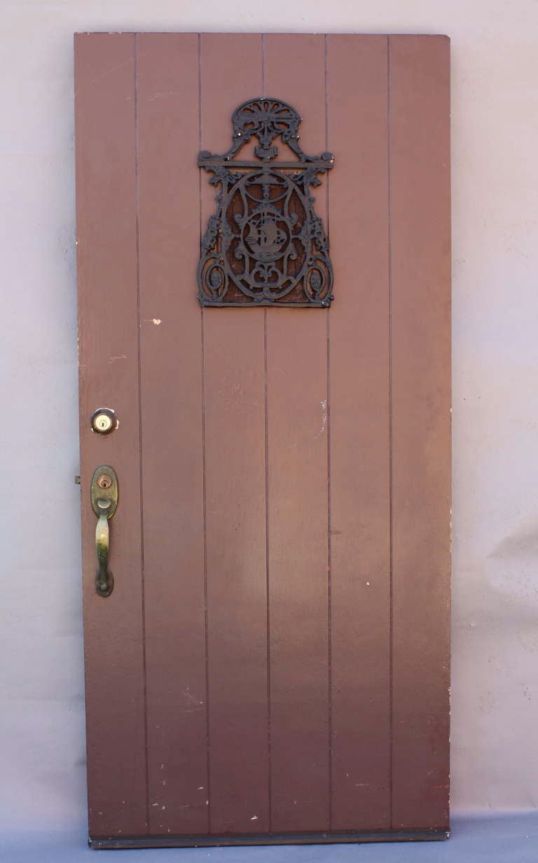 Wonderful wide-plank door c. 1920's with cast iron grill featuring a Spanish galleon at sea within ornate framework. Reverse reveals an interior hinged speakeasy door behind the grill. Original exterior handle and interior knob are present. A