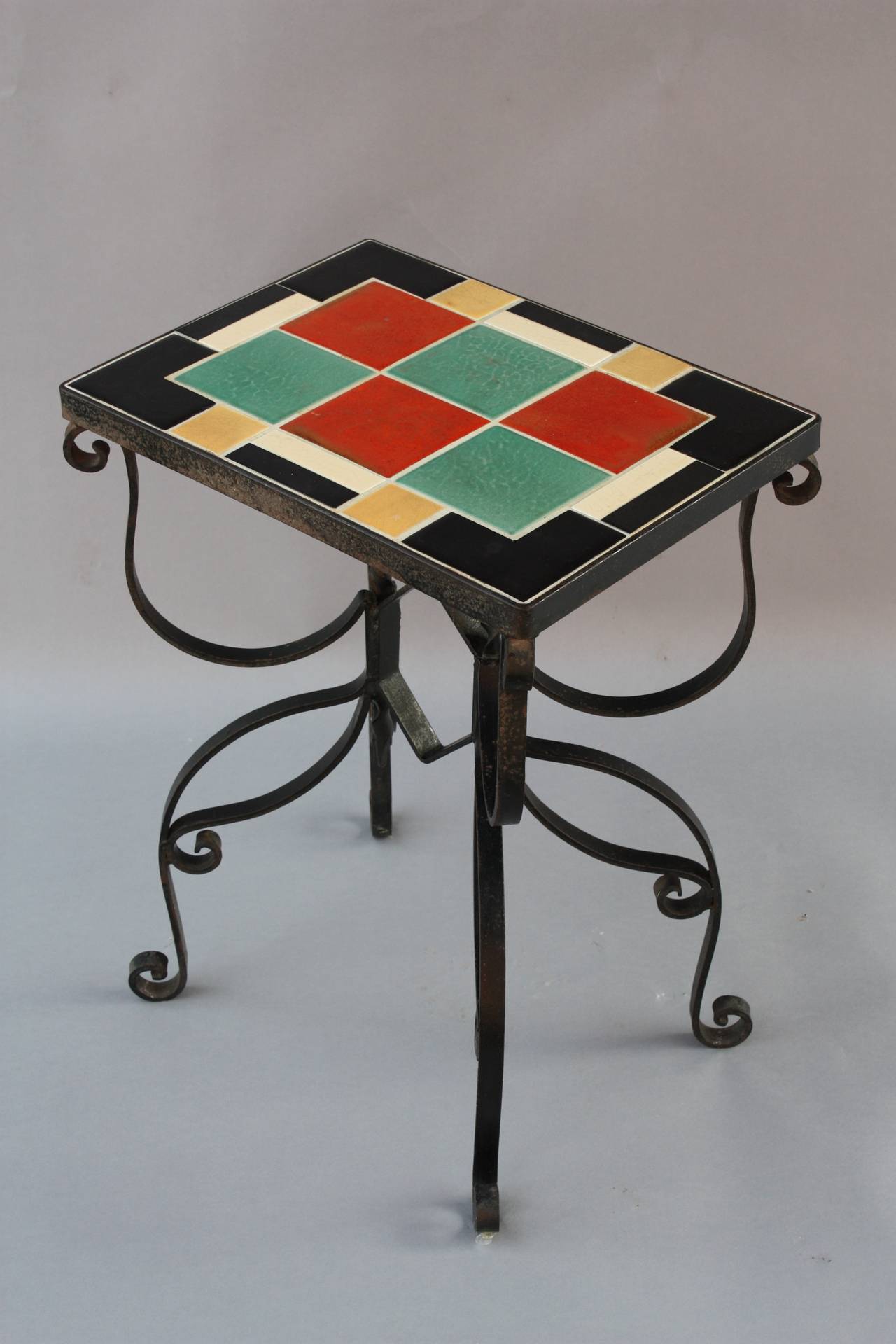 Nice, multi-colored tile table with hand-wrought iron base. The tile is made by the American Encaustic Co., Los Angeles. Measures 24
