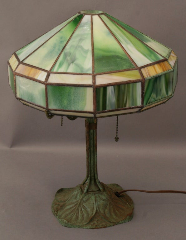 Stamped Bradley and Hubbard table lamp with bronze lily pad base and leaded slag glass shade in shades of green, white, and amber