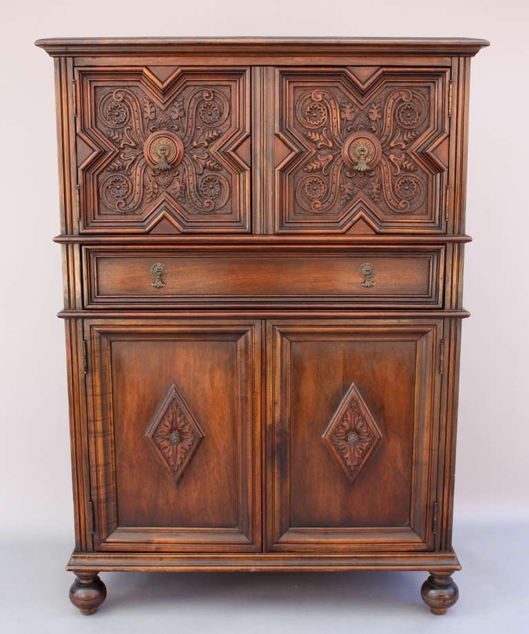 Spacious walnut cabinet with intricately carved face, c. 1920's. Single long drawer bisects two large open cabinet spaces with shelving.