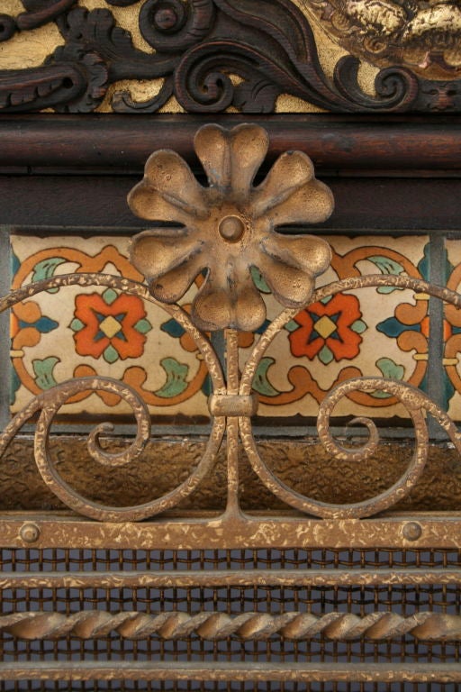 A beautiful marriage of period pieces that date from the 1920's era make up this wonderful fireplace mantle.  It features period Malibu tiles atop an ornate, hand-forged ironwork firescreen, and surrounded by intricately carved and guilt wood