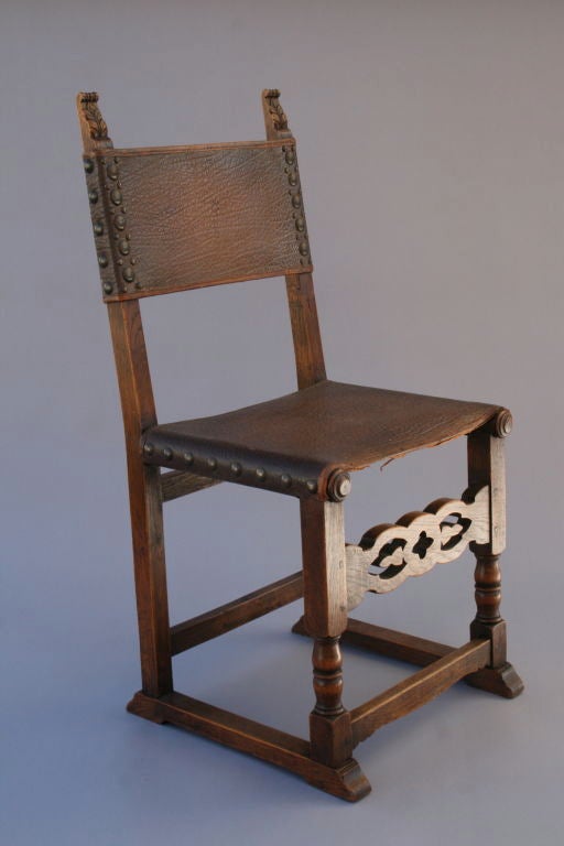 Set of six classic Spanish Revival dining chairs with original leather sling-style seats and brass nail heads. Simply carved decorative front stretchers add to the understated design.