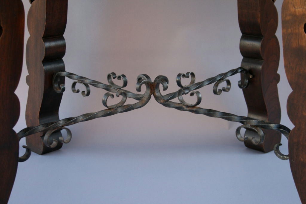 Square game table with thick, simply carved legs and decorative iron stretcher bars at center