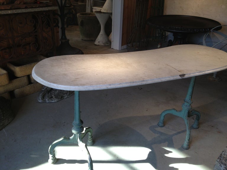 Dating to the late 19th century, this beauty features a large kidney-shaped and beveled-edge Carrara marble top atop a pair of trifid cast iron table bases welded together for a strong and durable structure. In wonderful old worn green paint with