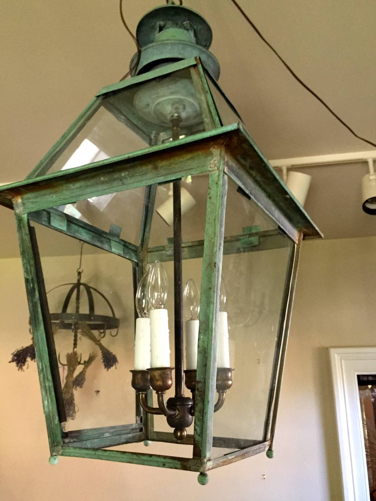 This beauty has an amazing naturally verdigris surface that only 100+ years of exposure to the elements can produce. Found in the US, but certainly English, we have electrified the lantern with a custom antiqued brass four-candle cluster with