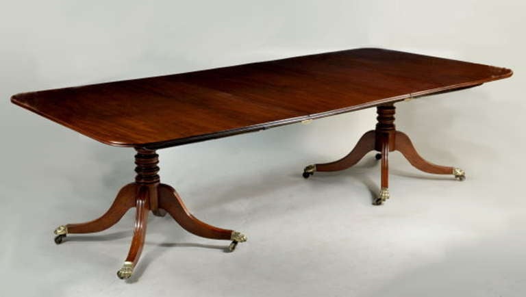 Very fine period Regency figured mahogany two pillar dining table, with double reeded edge tipping tops above baluster and ring turned columns, set on four arched molded legs ending in brass paw casters. England, circa 1815-1820. 