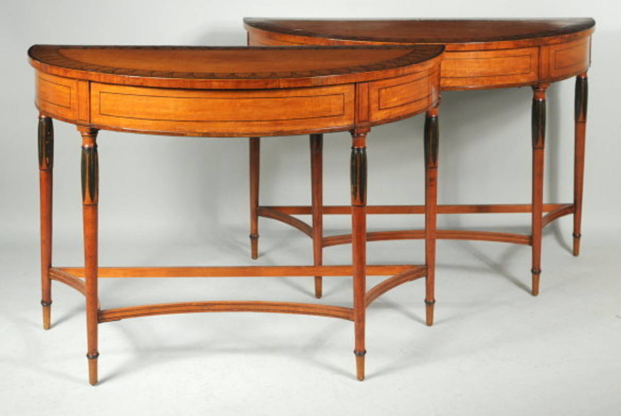 Very fine pair of George III paint decorated satinwood demilune console tables, half round form with anthemion and floral decorated top with crossbanded edge, above an apron with figured satinwood and string inlaid details, turned round legs with