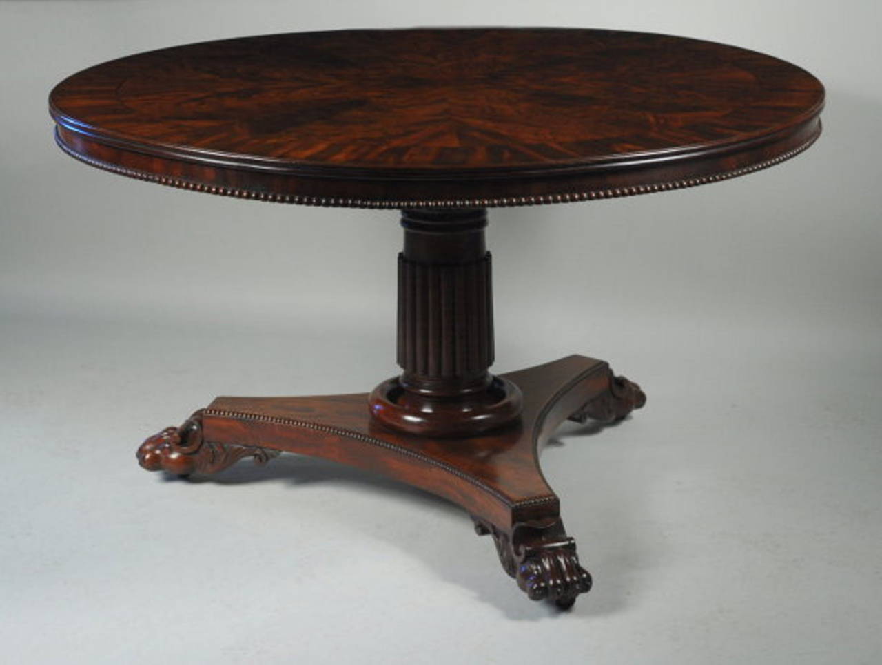 Exceptional Regency round library or center table with radiating
pie wedge figured mahogany veneered top with crossbanded edge, above a shallow apron with carved lower edge, tipping on a turned and reeded column supported on a triangular plinth