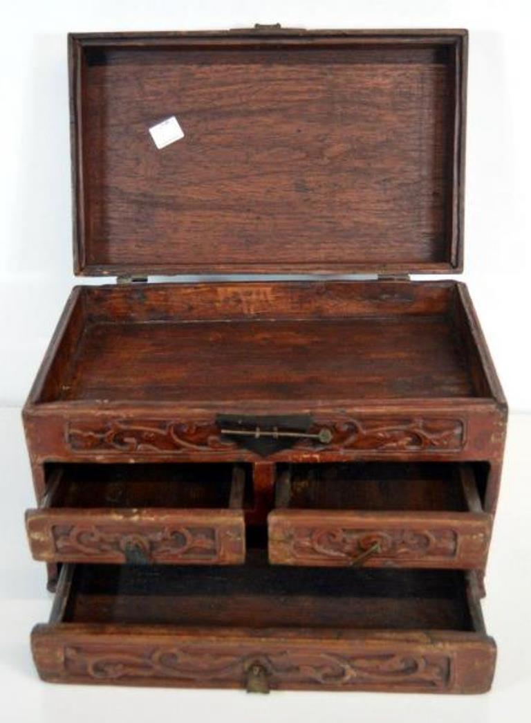 An early 20th century Chinese jewelry box made with red brown lacquered wood and iron hardware. This small rectangular box features a large bottom drawer, two smaller ones and a hinged lid. The front is blanketed with carved foliage patterns. Each