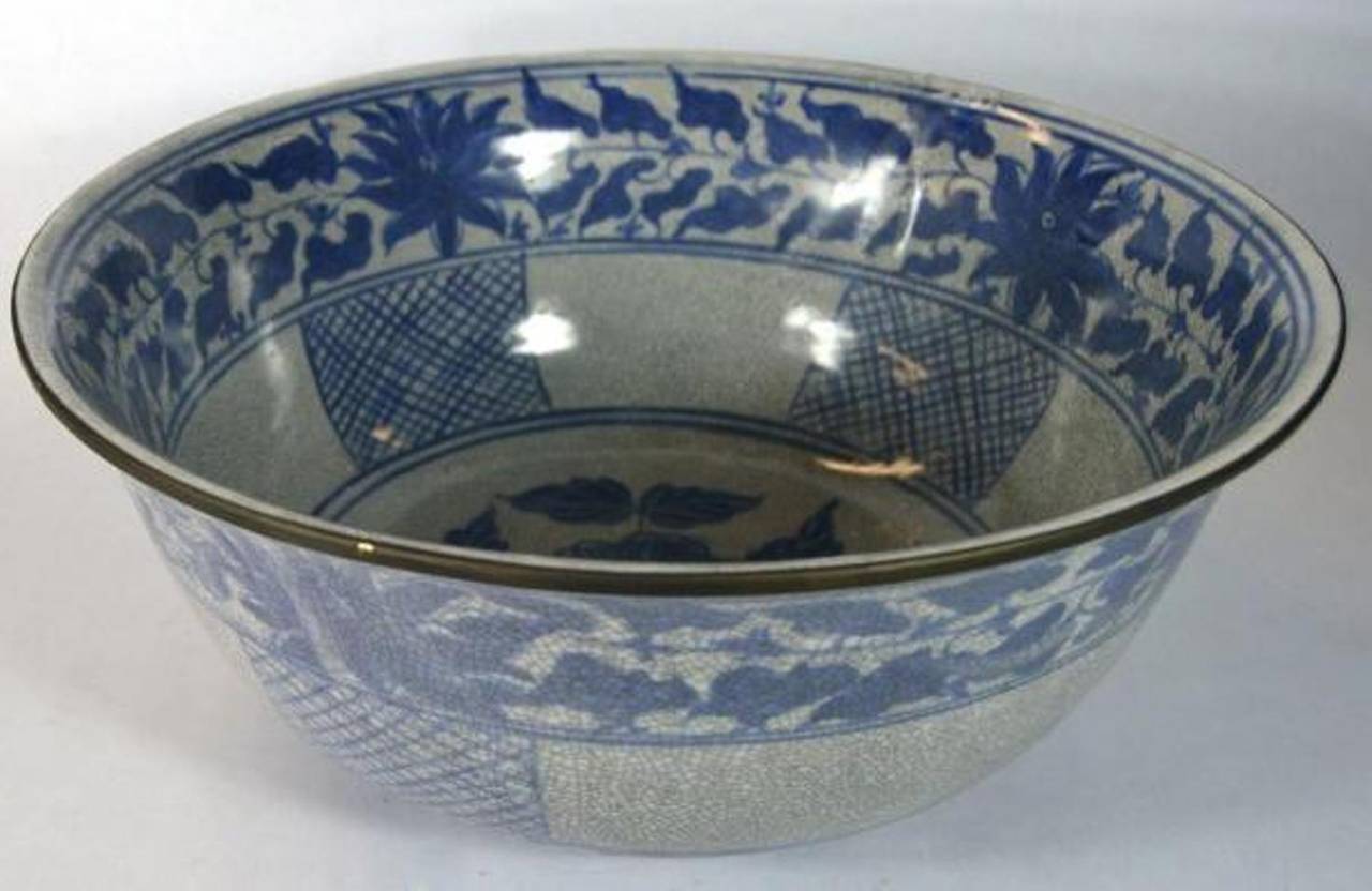 A 20th century Chinese wash basin made with blue and white porcelain and showcasing a crackle patina. The basin adopts a wide opened shape. The edge and the foot feature a dark painting detail. This wash basin displays a three-section adornment with