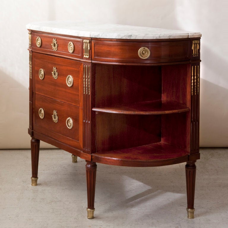 A Louis XVI period mahogany demilune cabinet, 3 central drawers, with 2 side drawers, gilt bronze mounts, with a fitted white marble top, ipen sides with shelf, French, late 18th century
