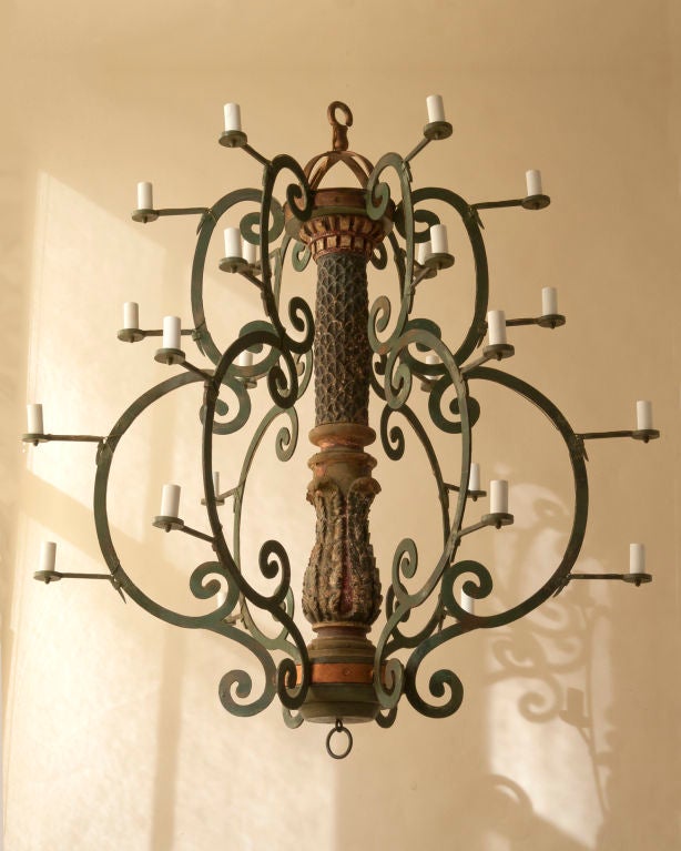 An unusual Baroque style iron and carved wood chandelier with votive candles, with a central carved shaft with six green painted scrolling arms, 24 lights,Continental,