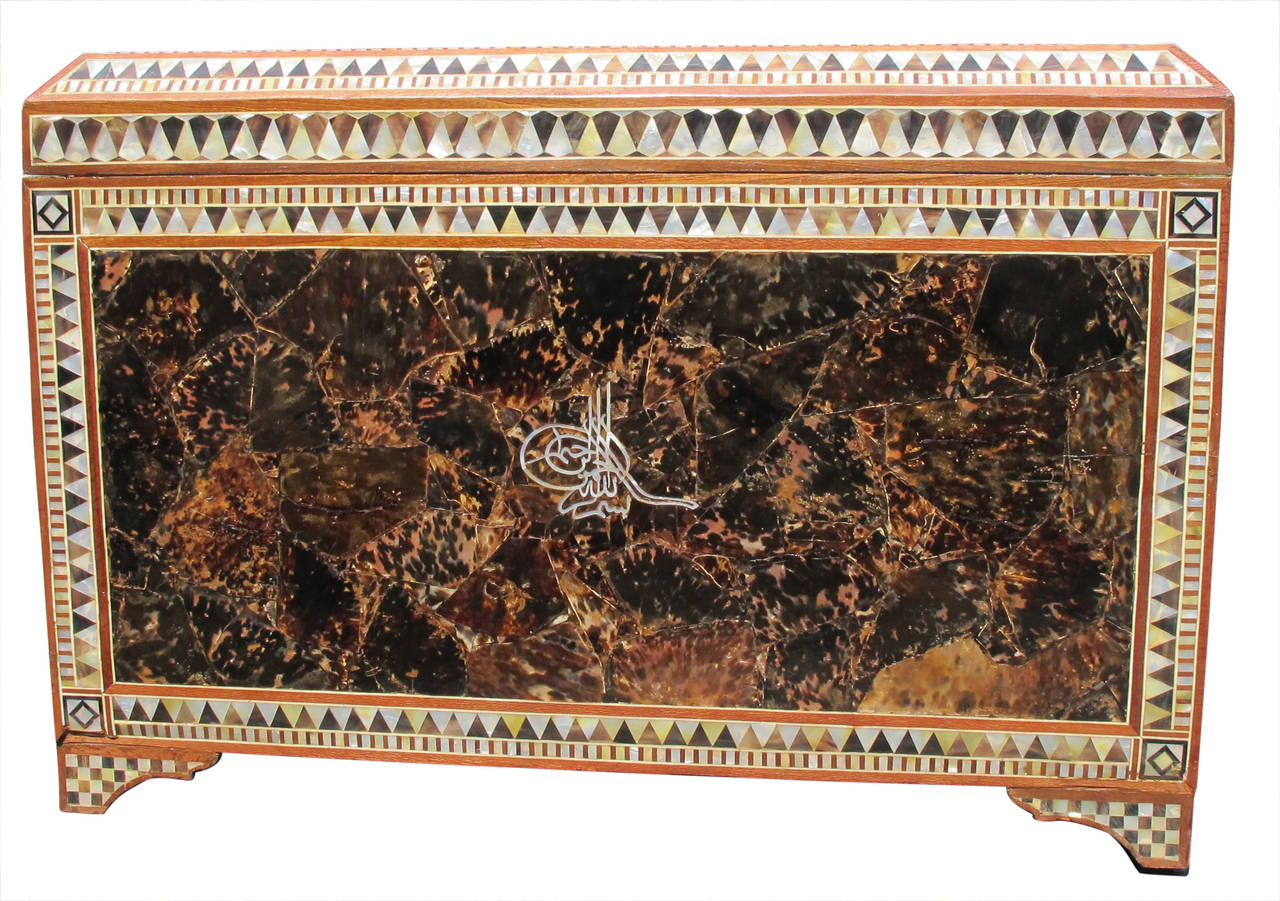 Of rectangular form on raised legs  and hinged lift top lid, the surface covered in inlaid mother-of-pearl and marquetry panels in diamond and triangular geometric shapes. Lid with geometric border with central script, edges with band of inlay.