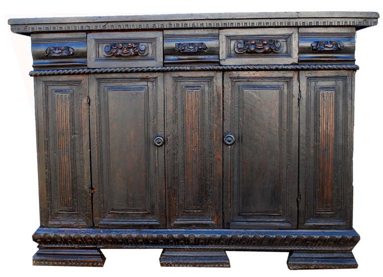 Exceptionally rare and very early Italian credenza. 16th Century or potentially earlier. Plank top with dentil molding, pair of paneled doors with interior shelf. The drawers are composed of carved figural elements. Beautiful original feet with
