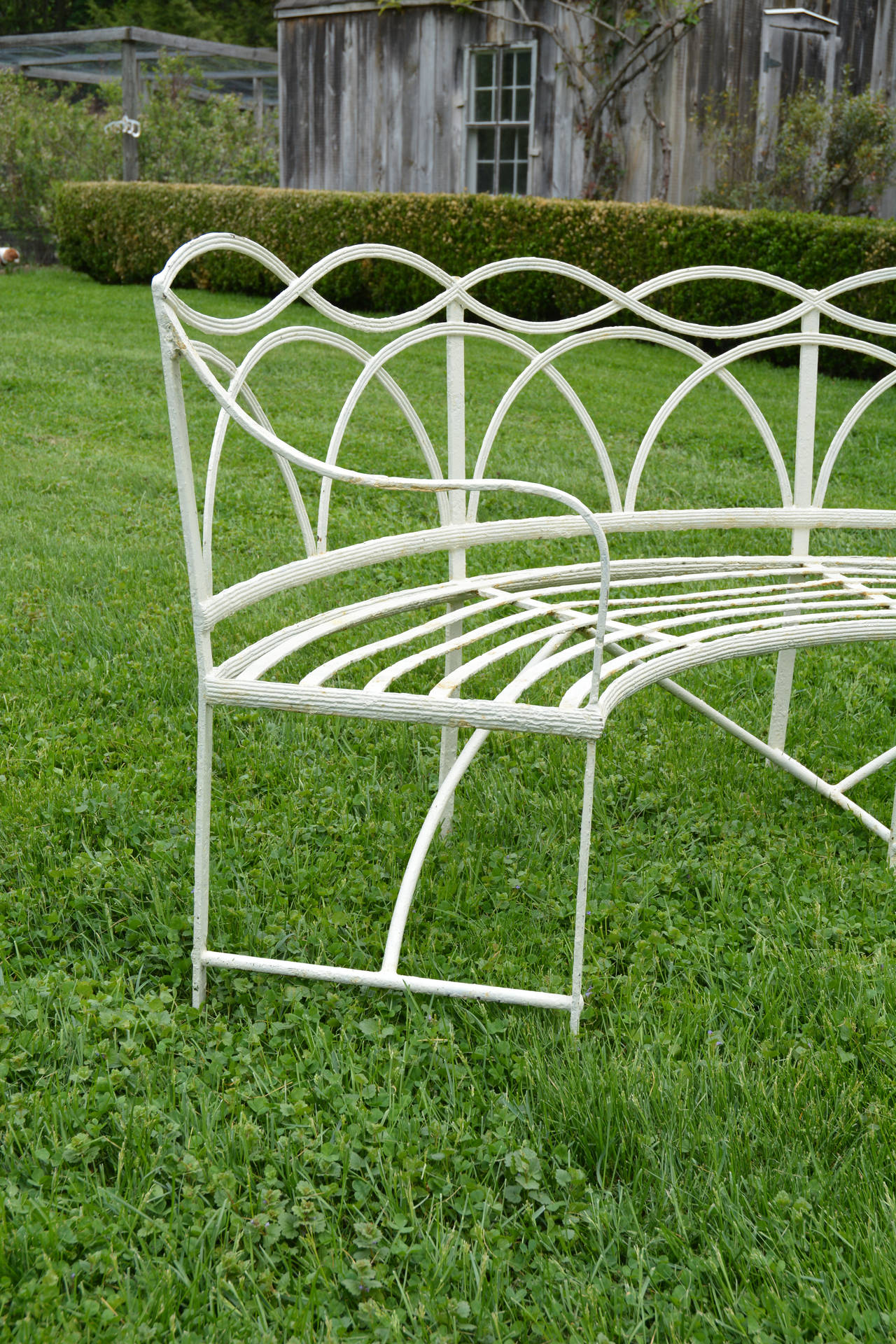 A pair of wrought iron semi-circular Regency garden seats, with reeded slats and paw feet.