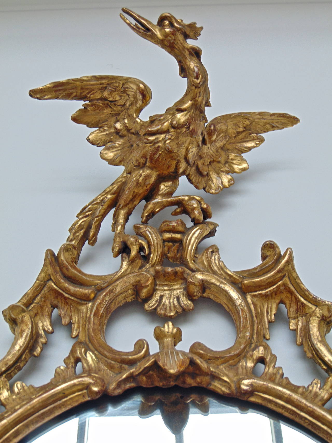 Exquisitely carved and executed giltwood oval Chippendale mirror.

--Carved foliate and rock Formations, C and S-scrolls, ho ho bird crest.
--Excellent old if not period gilding, cleaned and intact.
--Original backboards and surface.

--Most