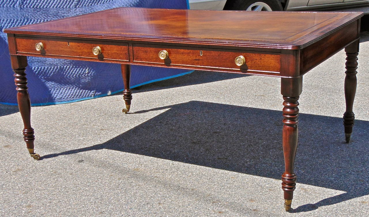 Beautiful mahogany Regency period writing desk or library table.

--Mellow brown tooled leather writing surface.
--Four turned legs on original brass casters.
--Two drawers on one side and two original 