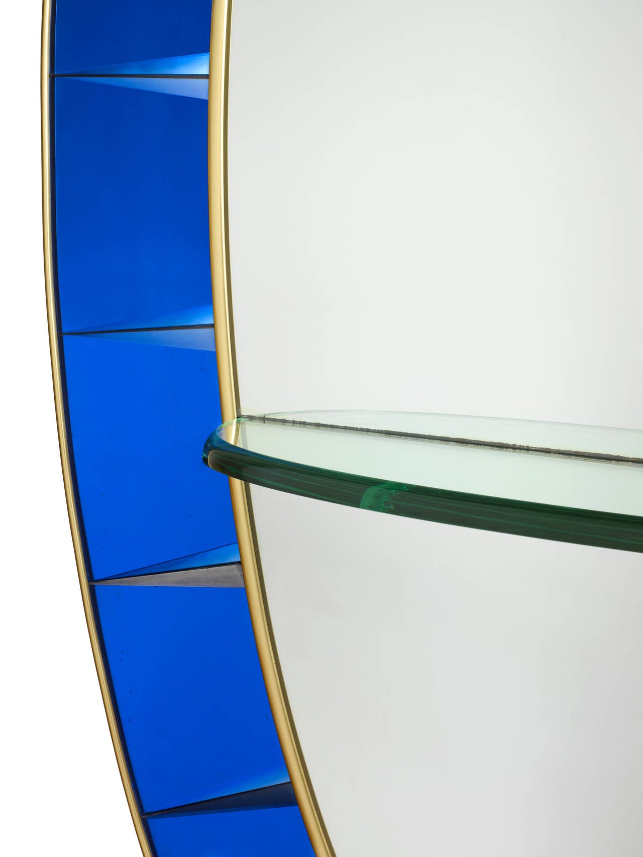 A full height oval mirror bordered with panels of cobalt-blue glass in a brass frame, with a glass console shelf and resting on a scrolled metal stand.