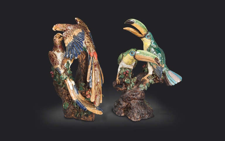 Two late 19th century majolica bird studies, attributed to Hugo Lonitz & Co, of a pair of toucans and parrots, each decorated in polychrome enamel work and shown naturalistically perched on tree trunk bases entwined with fruit and leaves. (O3D0240)